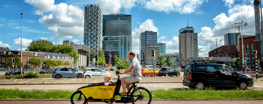Man met bakfiets en kind met de stad Utrecht op de achtergrond