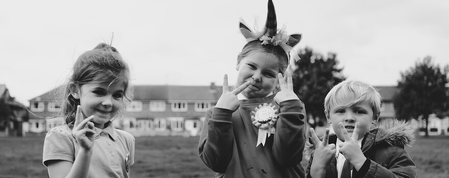 Een reportagefoto in zwart-wit van drie kinderen die buiten aan het spelen zijn en poseren voor de camera