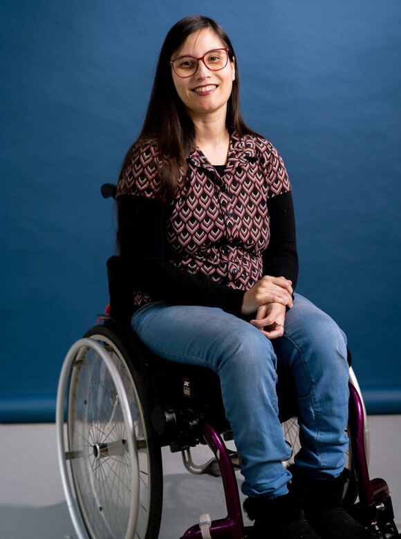 Arinda is een vrouw met zwart haar en een zwarte bril in een rolstoel 