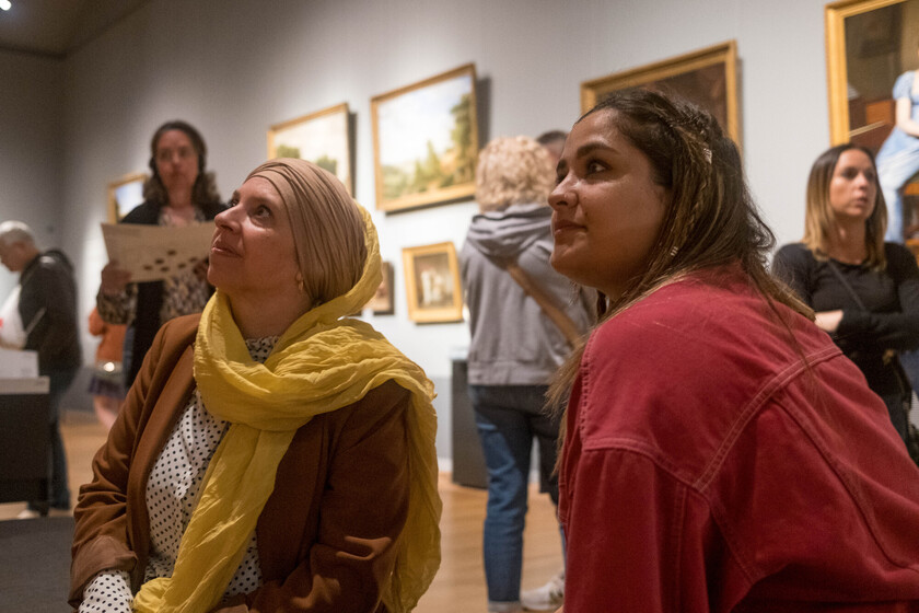 Twee vrouwen kijken omhoog, op de achtergrond zijn schilderijen te zien