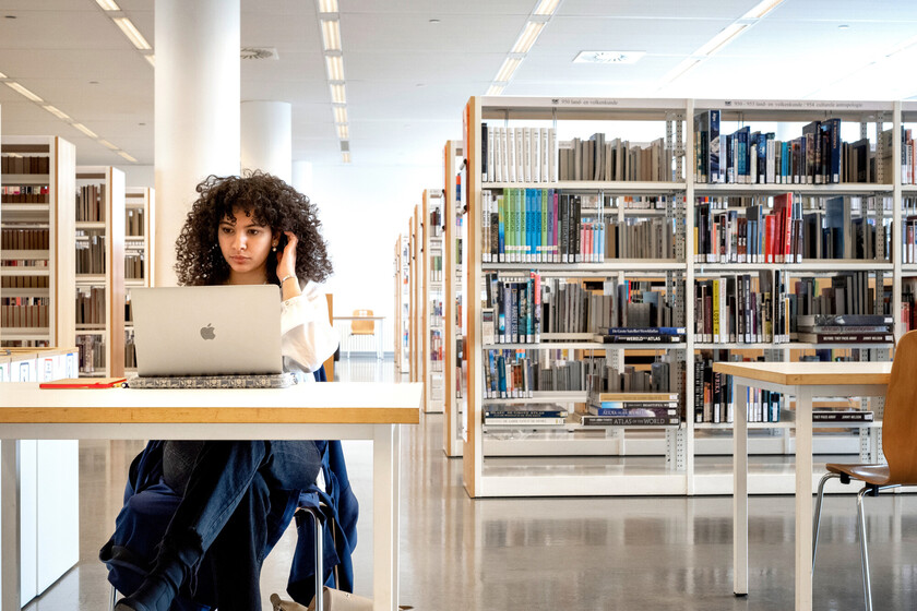 Vrouw zit in bibliotheek achter laptop