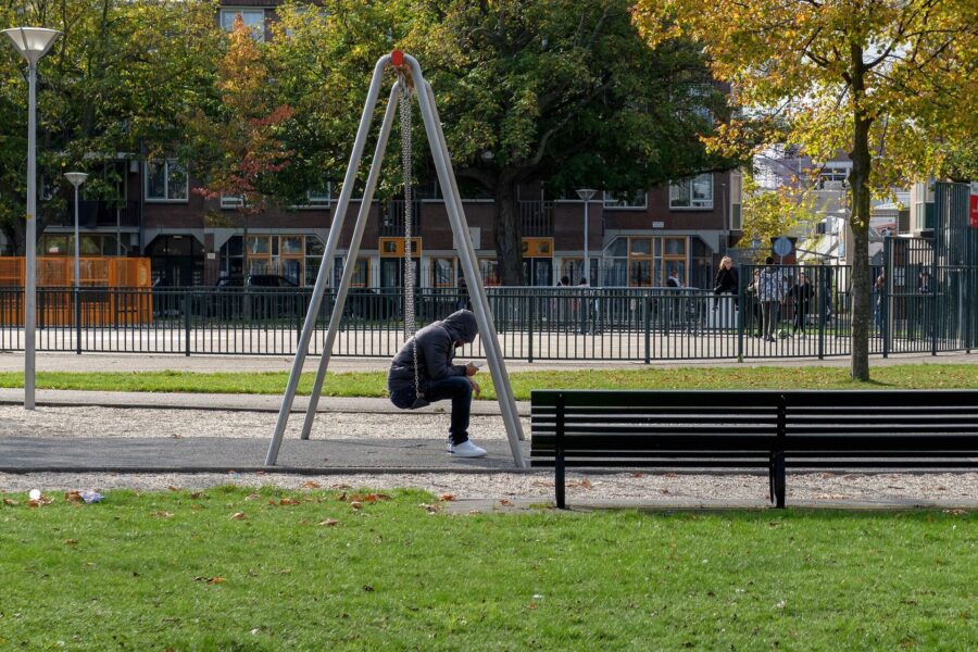 Jongere zit op een schommel op zijn telefoon