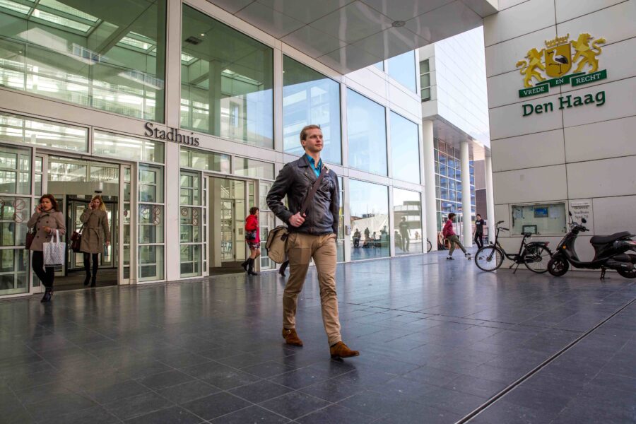 Een man loopt bij het stadhuis van Den Haag waar andere mensen op de achtergrond ook lopen.
