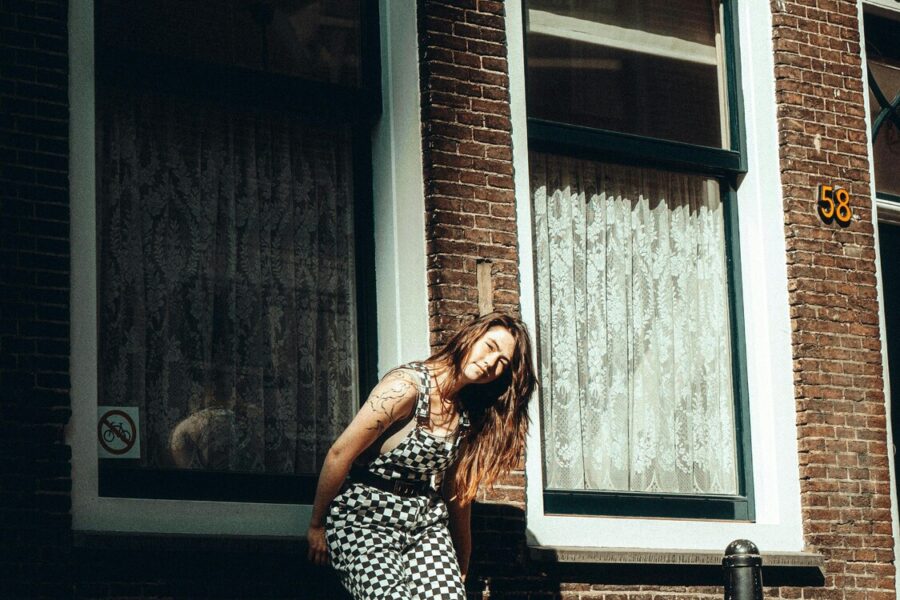 Een vrouw leunt tegen de kozijn van een raam bij een woning aan