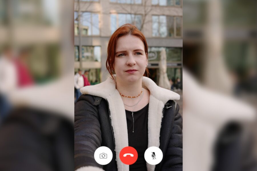 Een jonge vrouw loopt buiten en kijkt in de verte terwijl ze videobelt met iemand