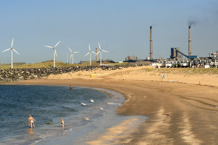 een gezin loopt op het strand naast tata steel en windmolens