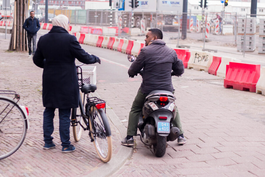 moslima vrouw praat tegen gekleurde man op scooter