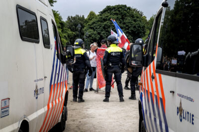 Twee politieauto's en een aantal politiemensen staan bij een groepje demonstranten die een Nederlandse vlag bij zich hebben